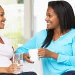 two woman talk on couch, one of them pregnant