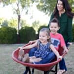 Young mother playing with children outdoors in wheelbarrow