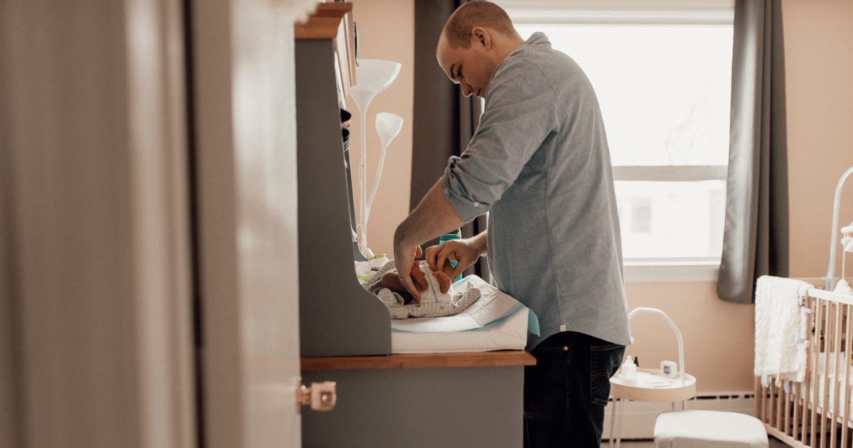 new dad changing baby's diaper at home in nursery
