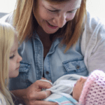 baby nurse holding baby with older sibling watching