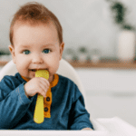 child sitting in high chair with spoon for solid foods