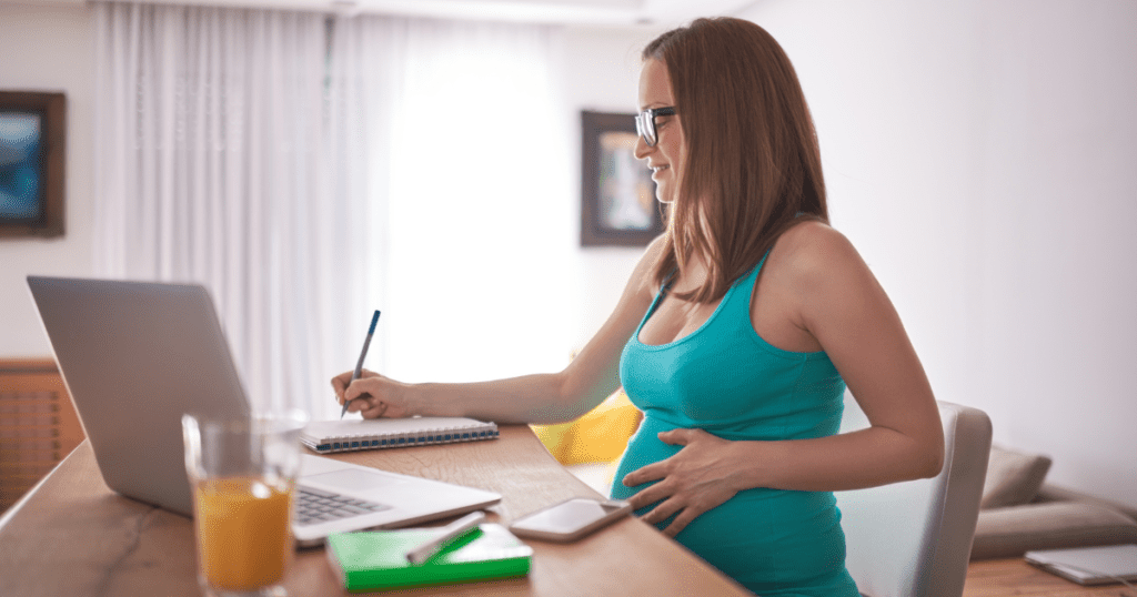 Pregnant woman at desk with laptop writing on checklist