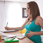 Pregnant woman at desk with laptop writing on checklist