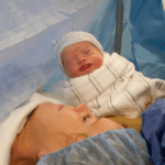 Newborn baby is presented to Mom on an operating table during a cesarean birth