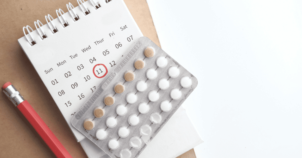 birth control pills on top of a calendar with a pencil