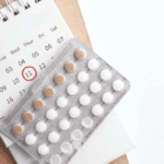 birth control pills on top of a calendar with a pencil