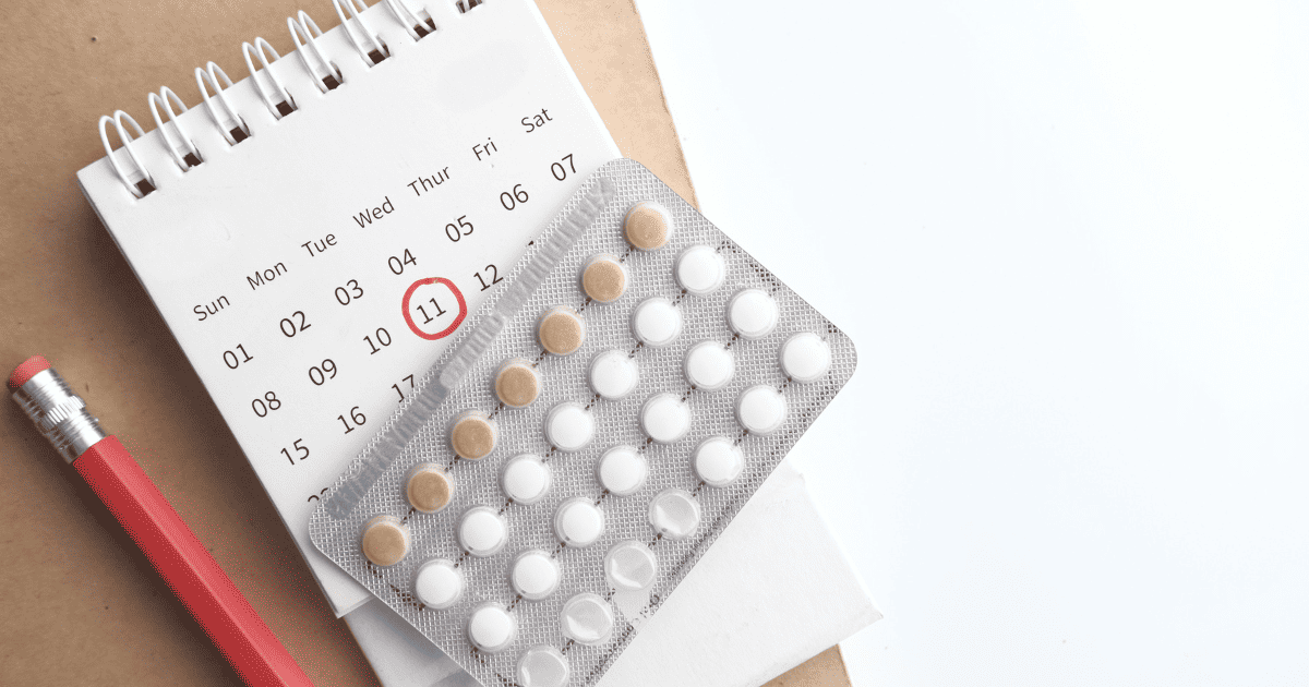birth control pills on top of a calendar with a pencil