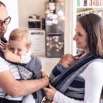 Two parents wearing their babies in a carrier and a wrap sling