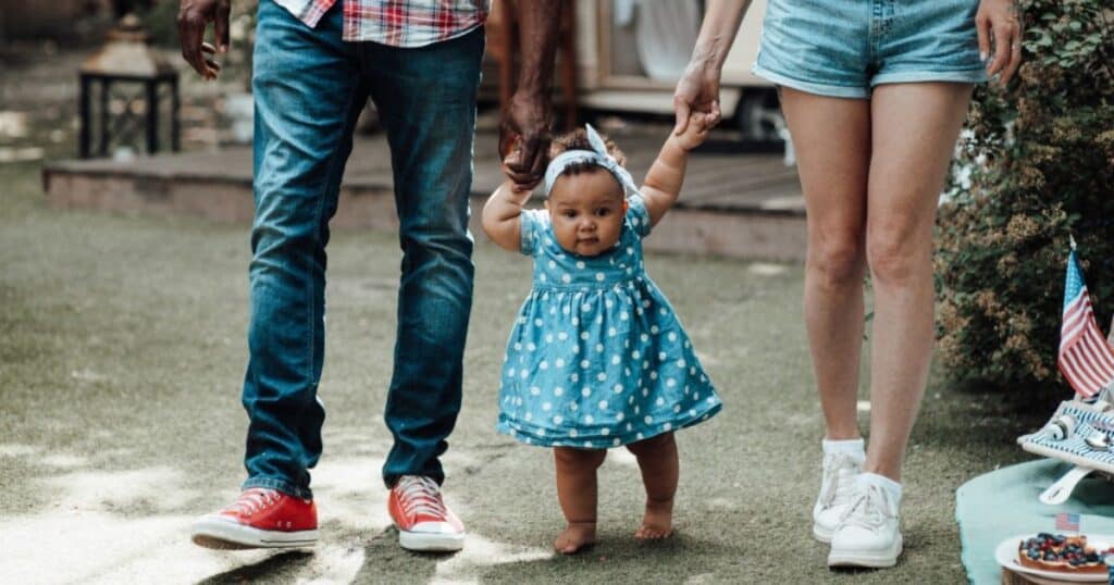 baby holding hands of parents walking