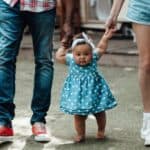 baby holding hands of parents walking