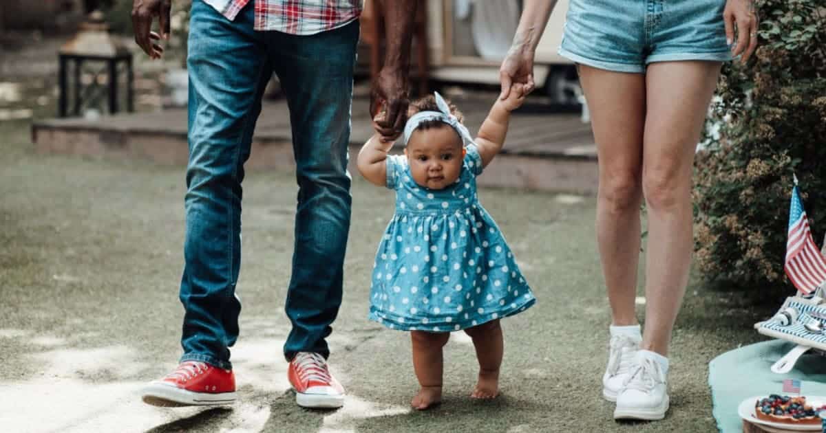 baby holding hands of parents walking