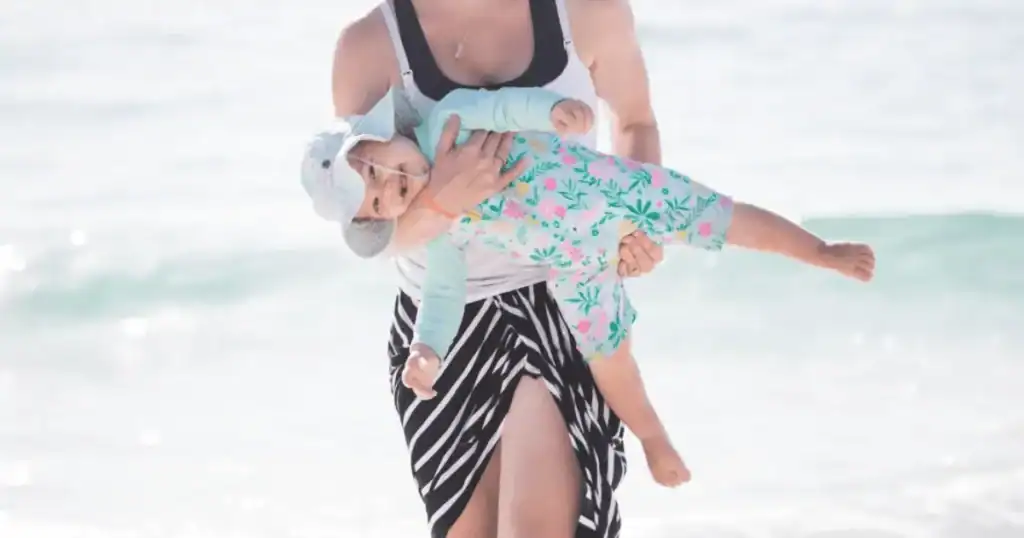 woman carrrying young baby in arms in sun suit at beach