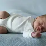 newborn baby sleeping on mattress in onesie