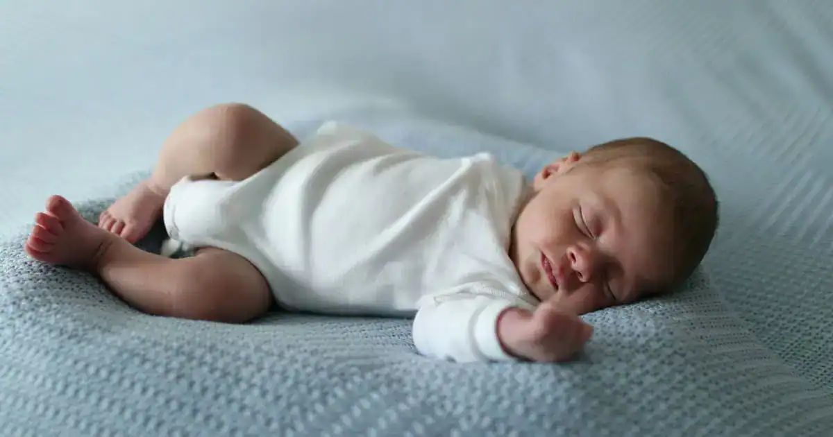 newborn baby sleeping on mattress in onesie