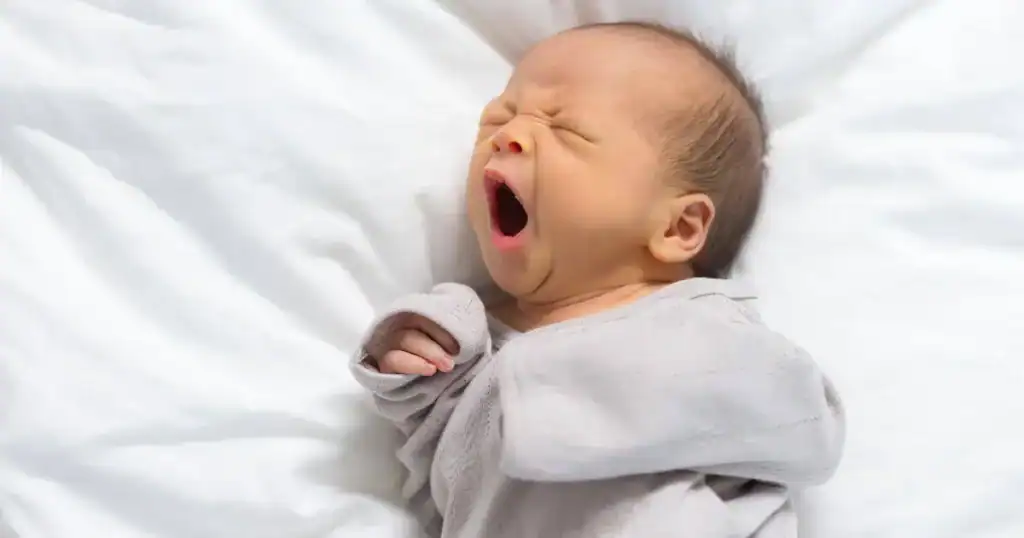 Newborn baby yawning while lying on a white blanket.