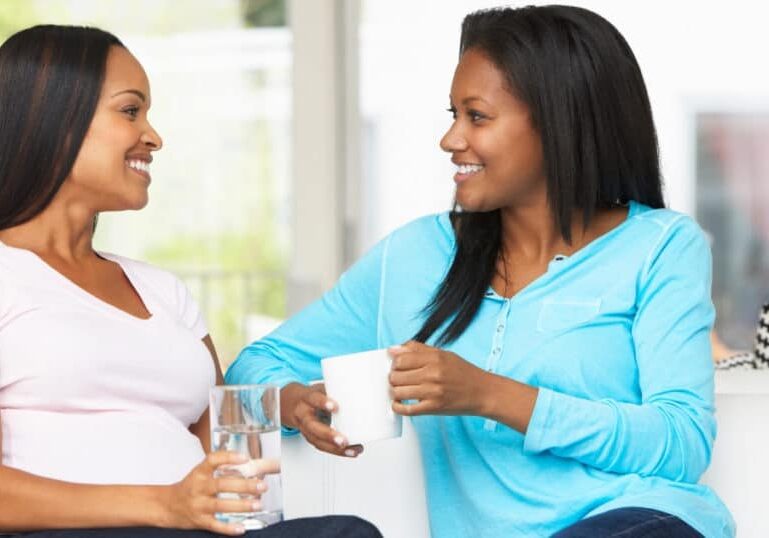 two woman talk on couch, one of them pregnant