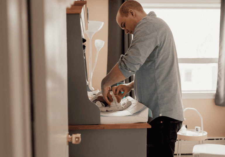 new dad changing baby's diaper at home in nursery