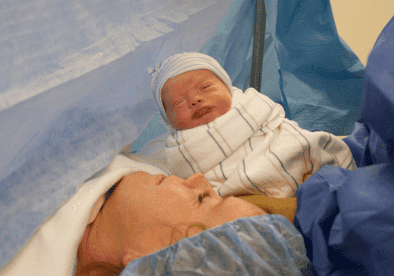 Newborn baby is presented to Mom on an operating table during a cesarean birth