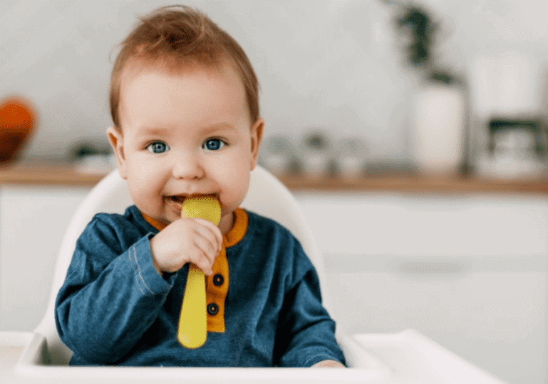 child sitting in high chair with spoon for solid foods
