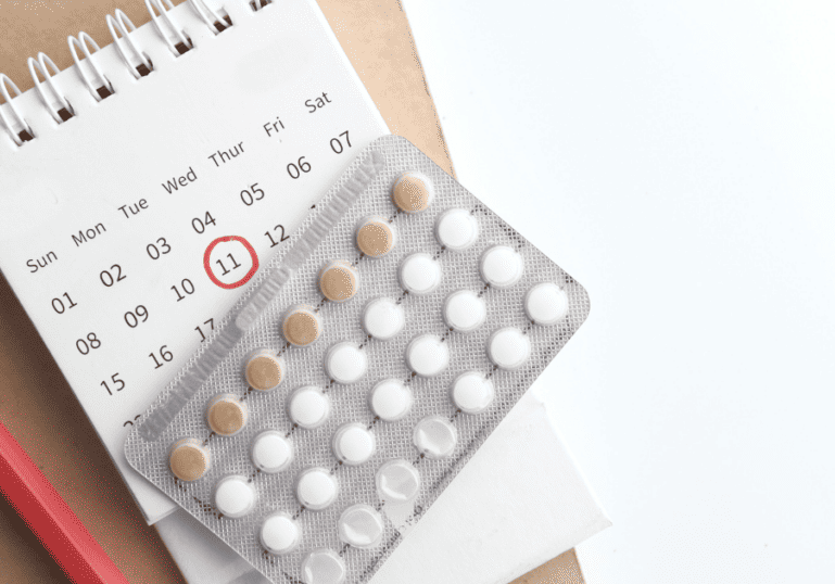 birth control pills on top of a calendar with a pencil