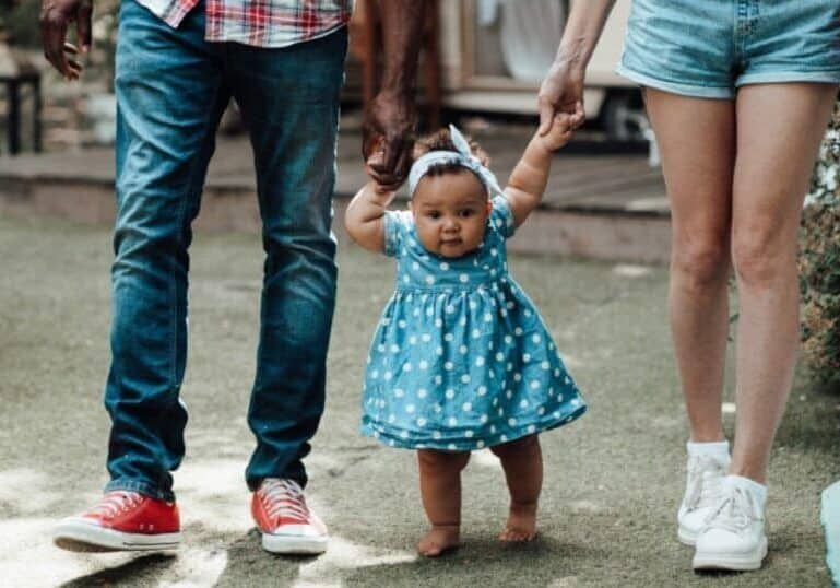 baby holding hands of parents walking
