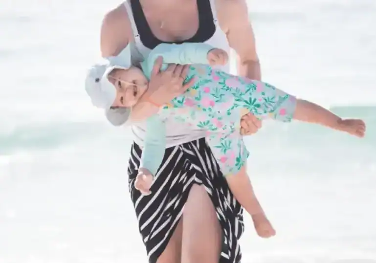 woman carrrying young baby in arms in sun suit at beach
