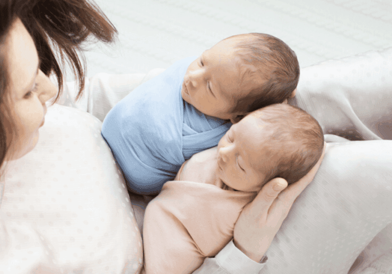 newborn swaddled twin babies with mother
