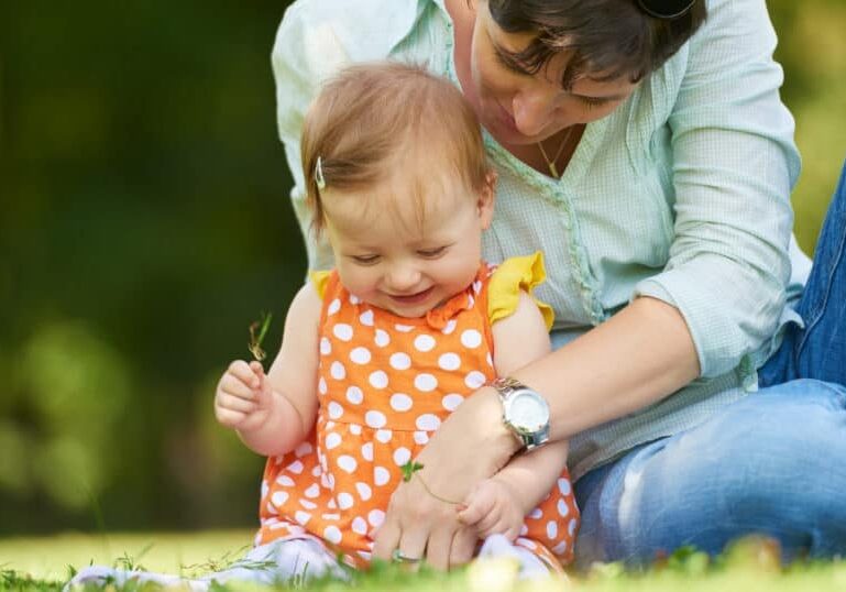 parent with baby in first year outside in grass