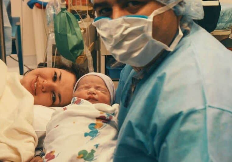 New parents in OR after cesarean birth holding newborn baby swaddled