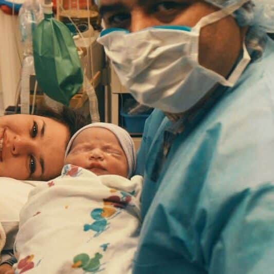 New parents in OR after cesarean birth holding newborn baby swaddled