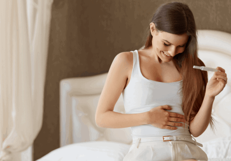newly pregnant woman holding pregnancy test and belly in first trimester