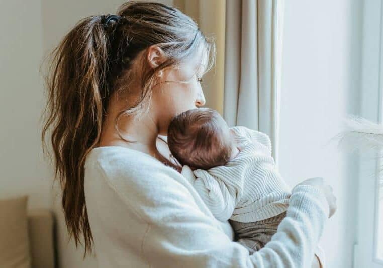 new mom by window postpartum holding baby
