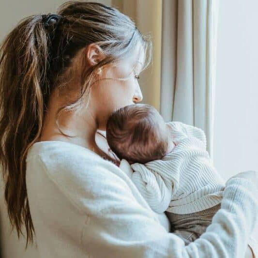 new mom by window postpartum holding baby