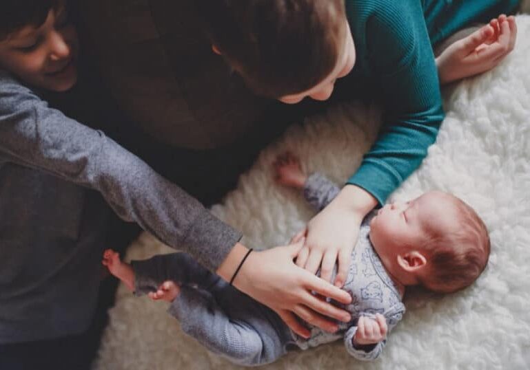 newborn baby being greeted by older siblings
