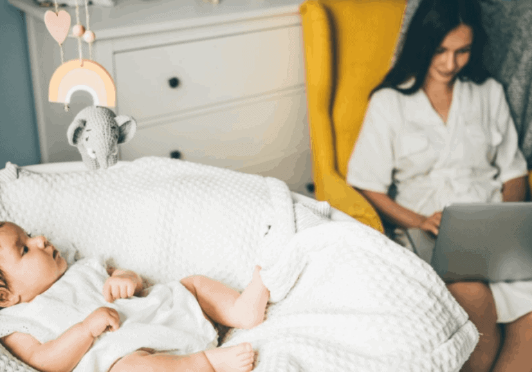 baby in cradle with mom working in chair by her side