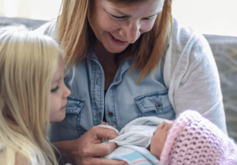 baby nurse holding baby with older sibling watching