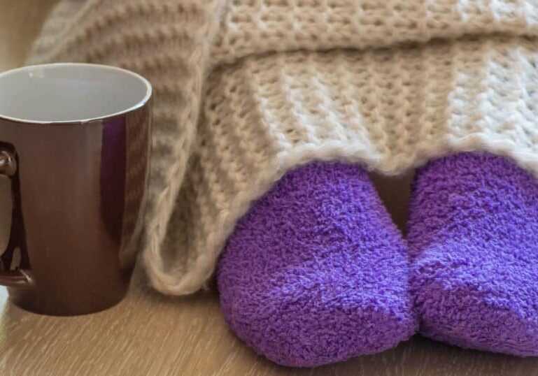 woman in cozy purple socks under blanket